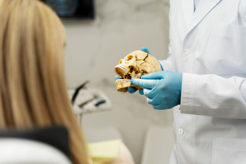 Prim-plan cu medic dentist care tine in mana un model de craniu, in timp ce explica cum apare resorbtie osoasa